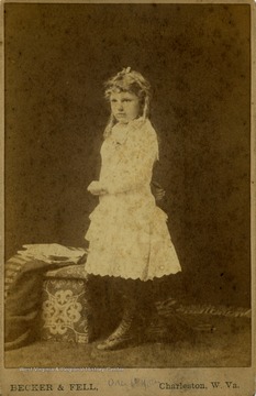 Cabinet card photograph of a young girl wearing Victorian style dress and high buttoned shoes.