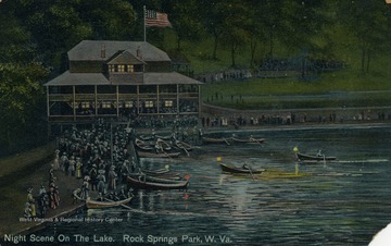 Lots of people gather around the boat dock and cabin to watch people arrive to shore in lit up canoes. See original for correspondence. Published by The Bagley Company. (From postcard collection legacy system.)