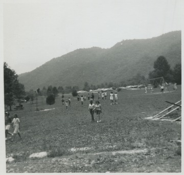 Parents and children walk across the field from the parking lot while others play on the swing set. 