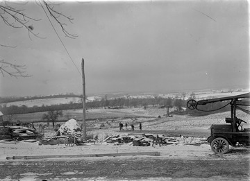 Timber and machinery to be used in community construction located in the foreground among snow covered ground.