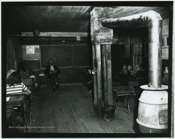 A teacher and his students of various ages, are pictured in a classroom. Subjects unidentified. 