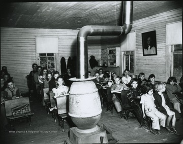 Children of various ages, sit behind their desks inside the classroom. Subjects unidentified. 