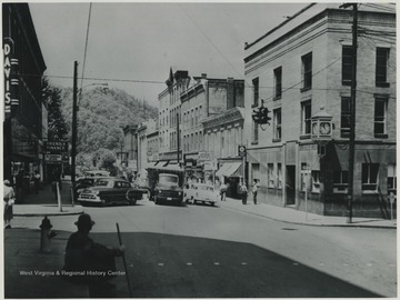 A truck passes by the line of parked cars. First National Bank building pictured on the right. 