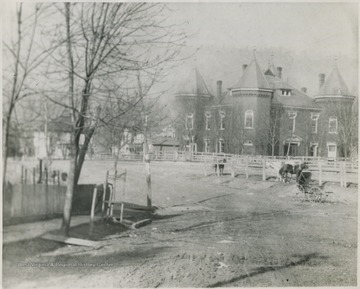 Looking at the building from across a field. A horse and old-fashioned baby stroller are pictured on the right. 