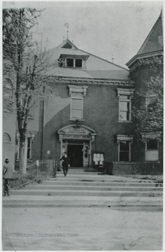 An unidentified man exits the courthouse, walking toward the steps that connect to the sidewalk.