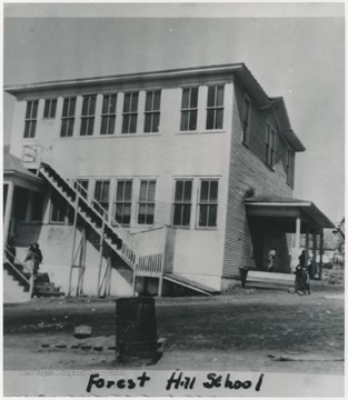 Looking at the school building from across the street. School children are pictured walked up the steps and around the building on either side. 