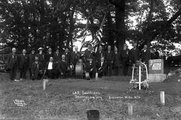 Veterans stand at grave site holding American flags.