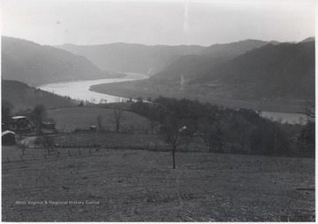 New River pictured winding through the valley. Two homes pictured by a dirt road. 