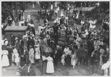 A crowd gathers across the lawn and surrounds the fountain pictured in the center. 