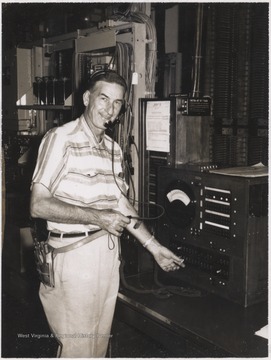 An unidentified man stands beside machinery while listening to headphones.