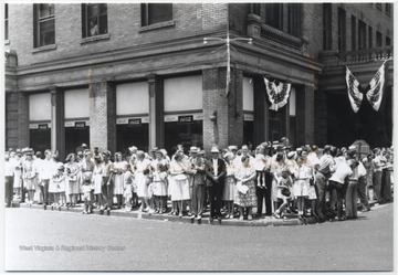 A crowd lines along the sidewalk as they eagerly await the procession. 