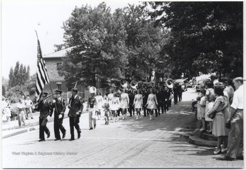 A marching band makes their way down a street lined with spectators. 