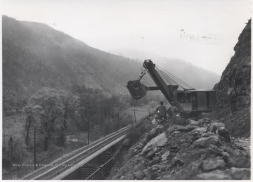 Two unidentified men watch as construction equipment puts the road together. 