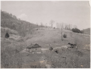 A log home sits beside a dirt path with a small shed.