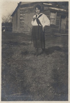 Wickline pictured next to a leafless, baby tree outside of a log cabin.