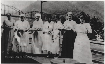 Seven unidentified women hold trays of food as they await the troops to pass through Hinton Station.