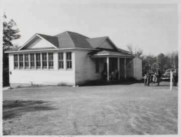 School children idle outside of the building with adults, perhaps their parents picking them up. Subjects unidentified. 