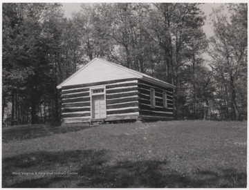 A small log building sits beside a forest. 