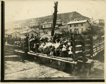 This image is part of the Thompson Family of Canaan Valley Collection. The Thompson family played a large role in the timber industry of Tucker County during the 1800s, and later prospered in the region as farmers, business owners, and prominent members of the Canaan Valley community.A group of people pose before an excursion to Blackwater Falls; the caption on the back of the print reads: "Vinegar Hill in background. These houses in back of Tannery. R.R. excursion toward Blackwater Falls."