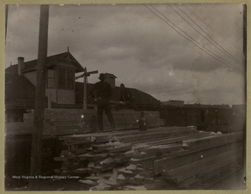 This image is part of the Thompson Family of Canaan Valley Collection. The Thompson family played a large role in the timber industry of Tucker County during the 1800s, and later prospered in the region as farmers, business owners, and prominent members of the Canaan Valley community.Two men standing on piles of lumber during the winter months at the Western Maryland Railroad Station in Davis, W. Va.