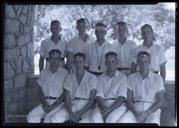 Eight male campers and their camp leader pose together outside of a stone building. 