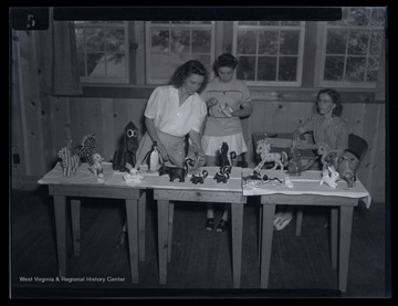 An unidentified girl places a finished toy product onto a table of toys. 