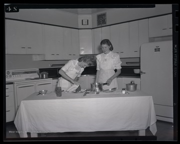 Two unidentified women show female campers how to correctly can beans. 