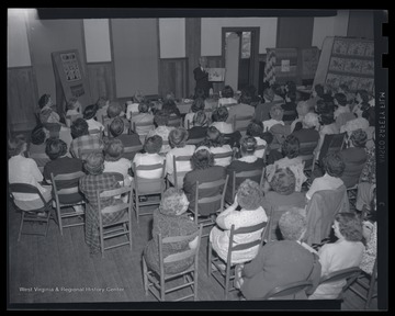 Eaton stands at the from of the room as he addresses a large group of women. 