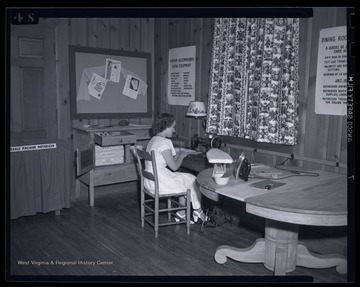 An unidentified girl sits at a sewing machine. 