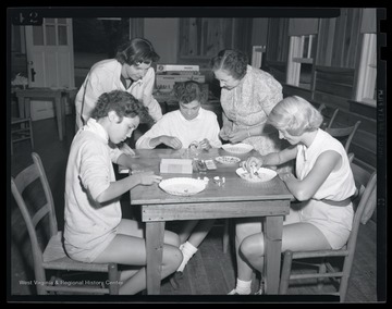 Two women supervise as three young girls paint bracelets. Subjects unidentified. 