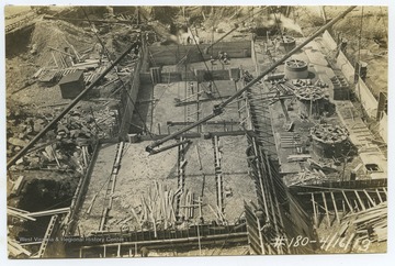 View overlooking the construction site, which is covered with equipment and building supplies. A group of workers work on various tasks.