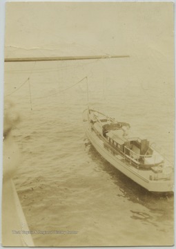 The motor boat that carries the officers to and from shore idles beside the battleship. 