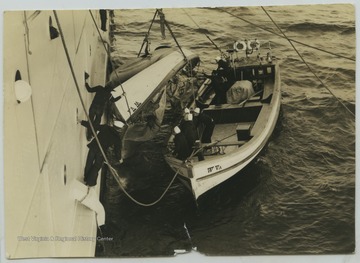 Crew members hanging out of the West Virginia and in a smaller boat alongside attempt to right the overturned boat.