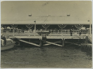 A crowd awaits the U.S.S. West Virginia crew returning from a voyage. The boat on the left is the captain's "gig."