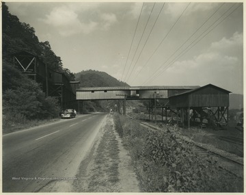 A man stands beside a parked automobile beneath the facilities. 