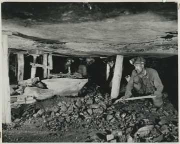 Four unidentified men shovel coal. 