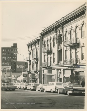 View looking south on High Street in Morgantown, W. Va.  Businesses visible include Jacobs Men's Wear, Stenger's News, Comuntzis, Mountaineer Sport Shop, Conners One Hour Cleaning, Electric Equipment Co., and others, as well as billboards advertising Coca-Cola and Orange Crush.  Photo taken for "Project 63," a revitalization project undertaken in the early 1960s.