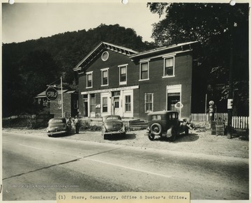 Two men stand outside of the building beside parked cars. 