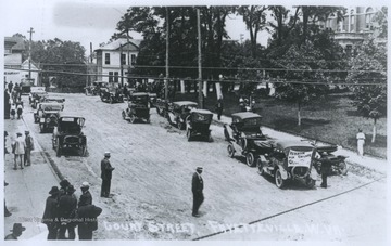 Cars are parked along the sidewalk where men and women walk about. The courthouse is visible to the left.