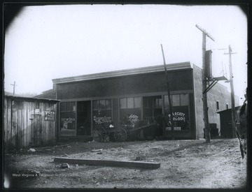 A horse-drawn carriage is pictured outside of the building's entrance. The saloon sits next to a barber shop, pool parlor, and lunch diner. 