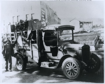 Mangen stands beside his truck on "moving day" in the coal fields. His truck holds a number of personal belongings, including a sewing machine, as well as a cow.