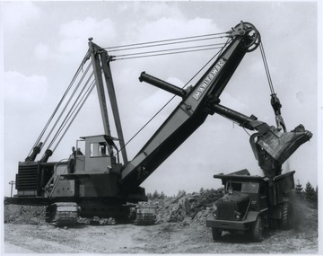 A power shovel dumps dirt into a truck. 