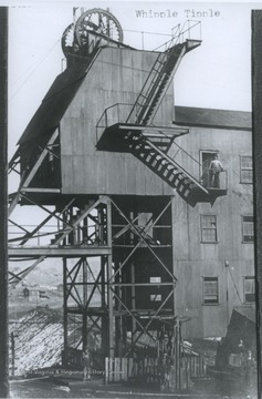 Three men stand beside the tracks while steam pours out of the building's many chimneys. 