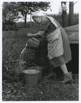 Mrs. Calvert dumps water into pails. She was living without running water.