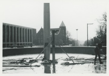 The installation of U.S.S. West Virginia's mast nears completion at Memorial Plaza on the campus of West Virginia University.  The Mountainlair and Stewart Hall are visible in the background.