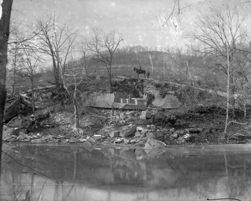 A man on a horse sits on top of a hill, where below there are stonemasons cutting into the rock. 