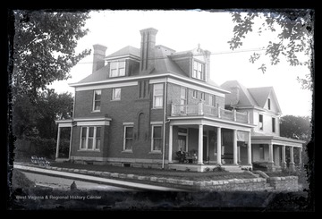 A man sits on the porch of the home in the forefront. The second house is under construction. 