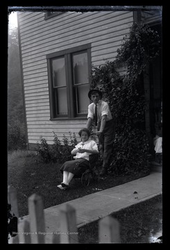 An unidentified boy pushes a young girl in a wheelchair across a lawn. 