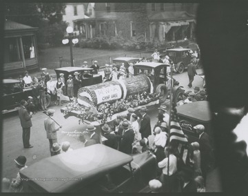 A crowd observes as the M. W. of A. float makes its way down the street.