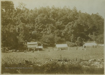 Tents are pitched across a field. A large American flag waves above banners that read, "Camp Wilson on the Cheat River" and "Grapeville Outing Club, Grapeville, Pa."